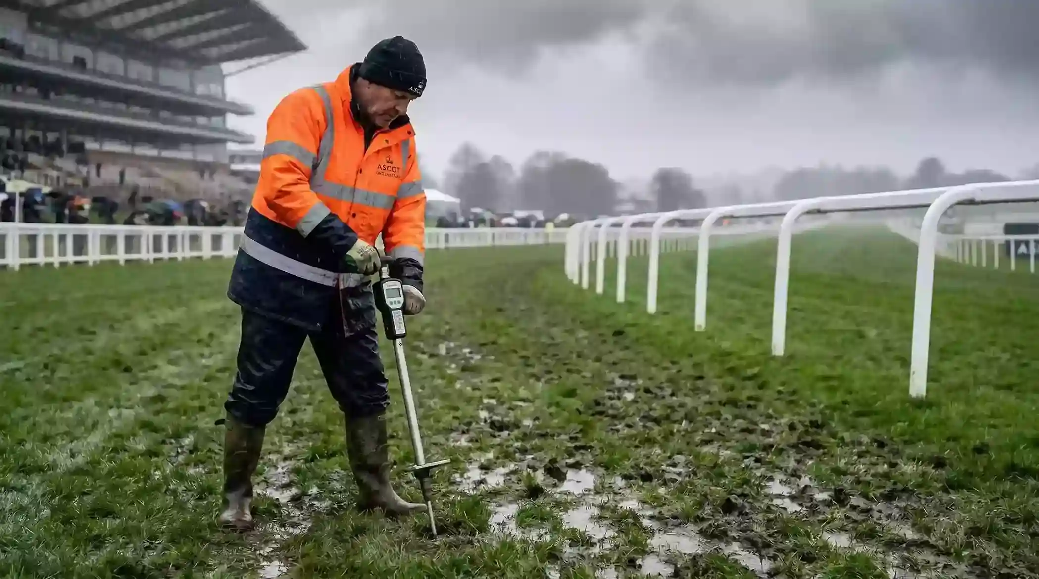 Groundsman testing soft turf with a going stick at a waterlogged UK racecourse